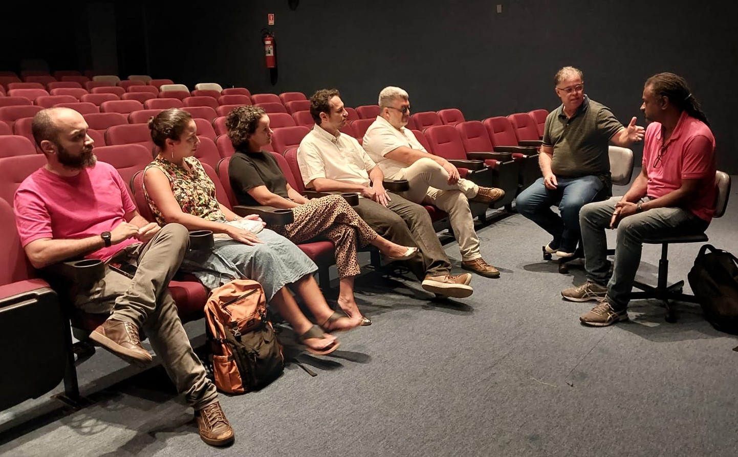 Foto da reunião, realizada no Cine Metrópolis, com todos os participantes sentados nas cadeiras do cinema