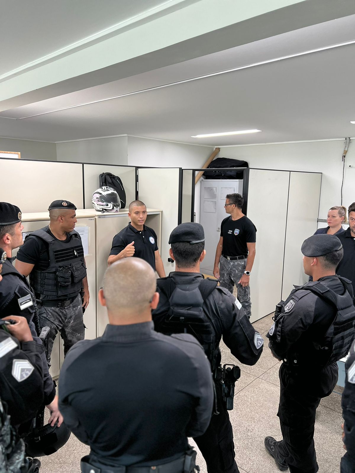 O pesquisador Geanderson reunido com um grupo de policiais em uma sala, todos em pé e usando farda preta.