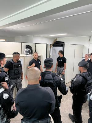 O pesquisador Geanderson reunido com um grupo de policiais em uma sala, todos em pé e usando farda preta.