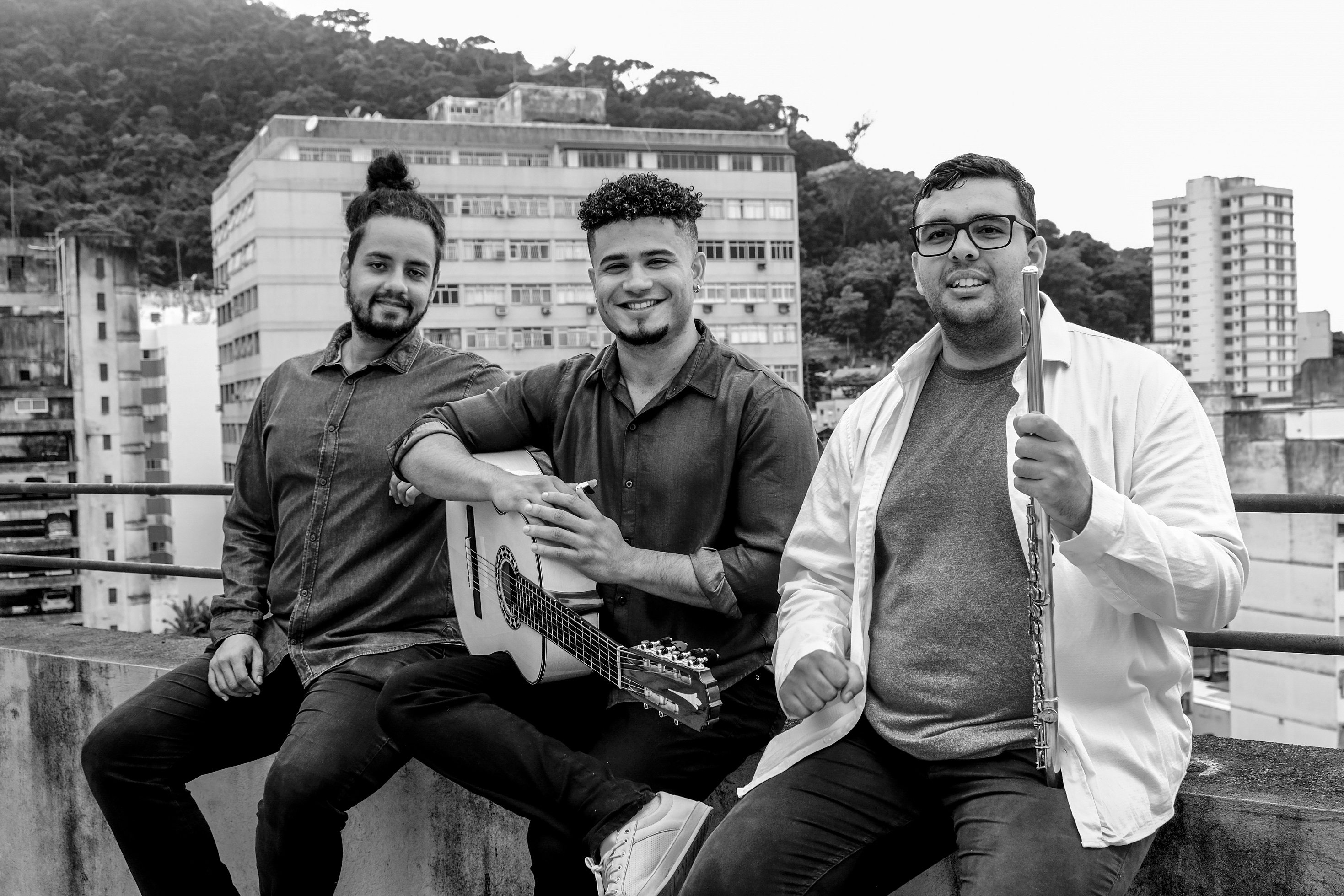 Foto em preto e branco de Léo de Paula, Luciano Furtado e Matheus Viana sentados na mureta de um viaduto, com prédios ao fundo.