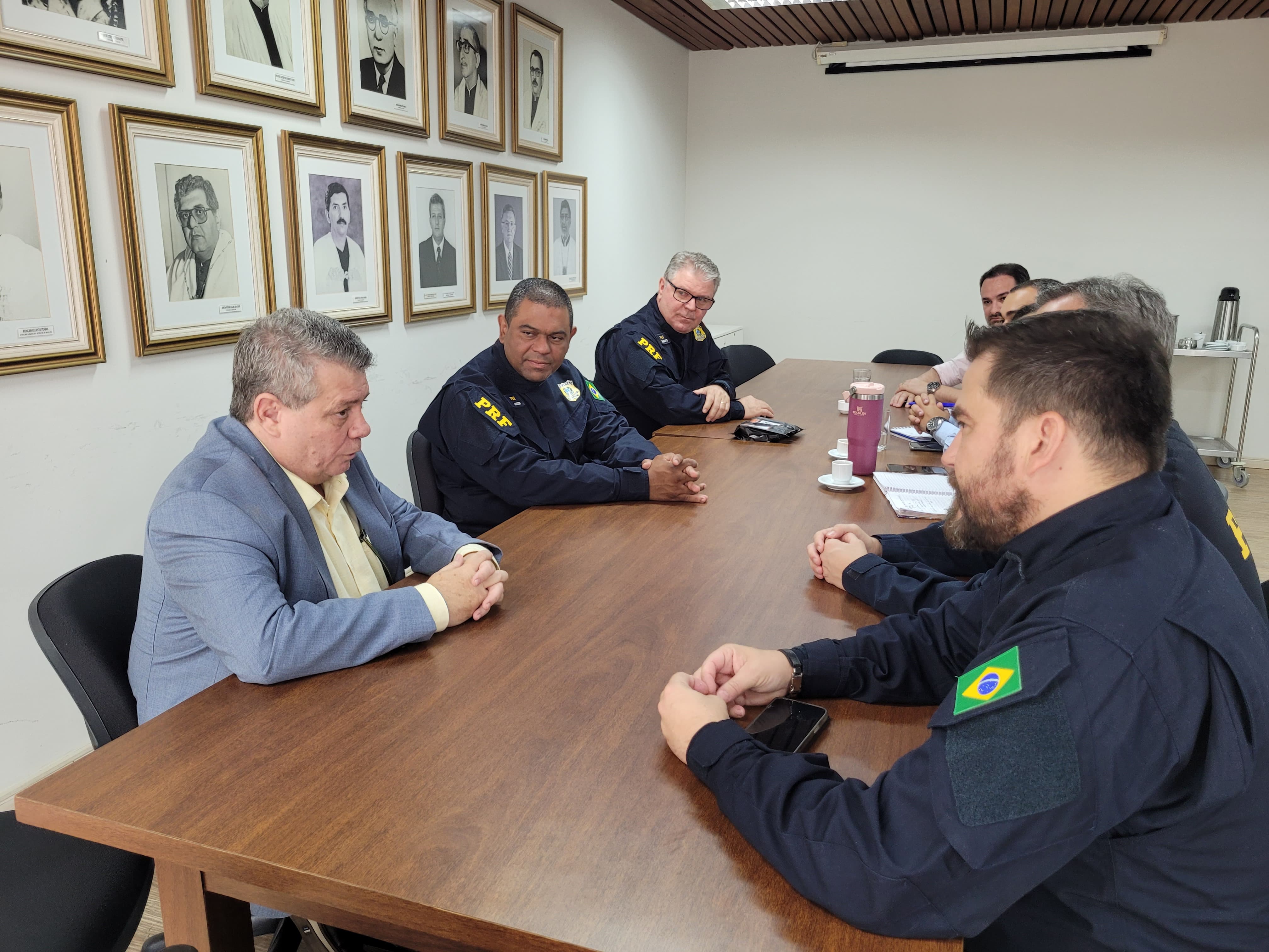 O reitor Eustáquio de Castro reunido com os policiais federais. Todos estão sentados em torno de uma mesa de madeira. Na parede, a galeria de fotos dos ex-reitores da Ufes.