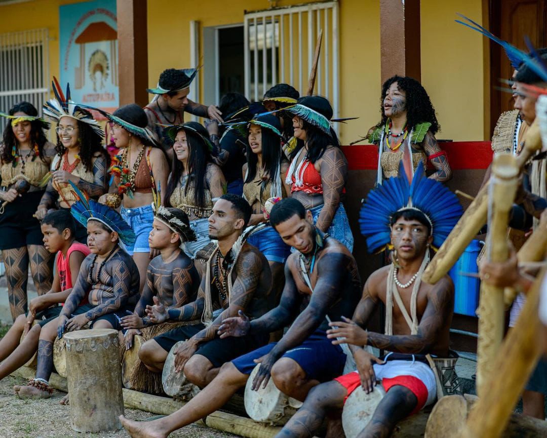 Grupo de dança Jovem Tupinikim, de Aracruz - ES. A foto mostra um grupo de jovens indígenas com os corpos pintados usando cocares e acessórios indígenas. Alguns tocam pequenos tambores.