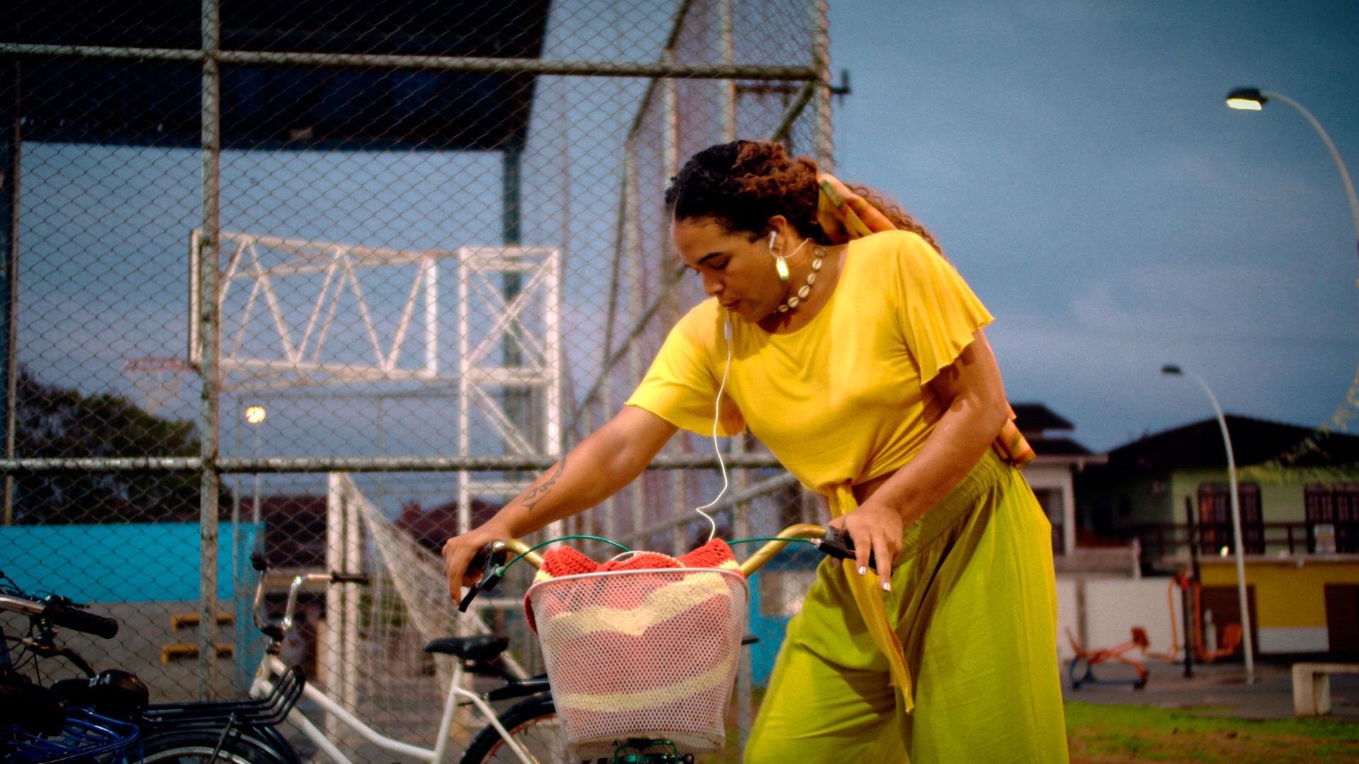 Imagem do filme sub(urbana) que mostra uma mulher em uma praça, se preparando para subir em uma bicicleta