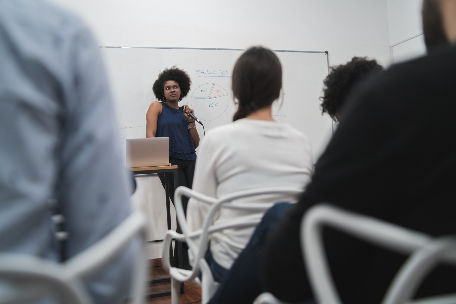 Imagem de uma mulher negra à frente de uma sala, falando para outros colegas