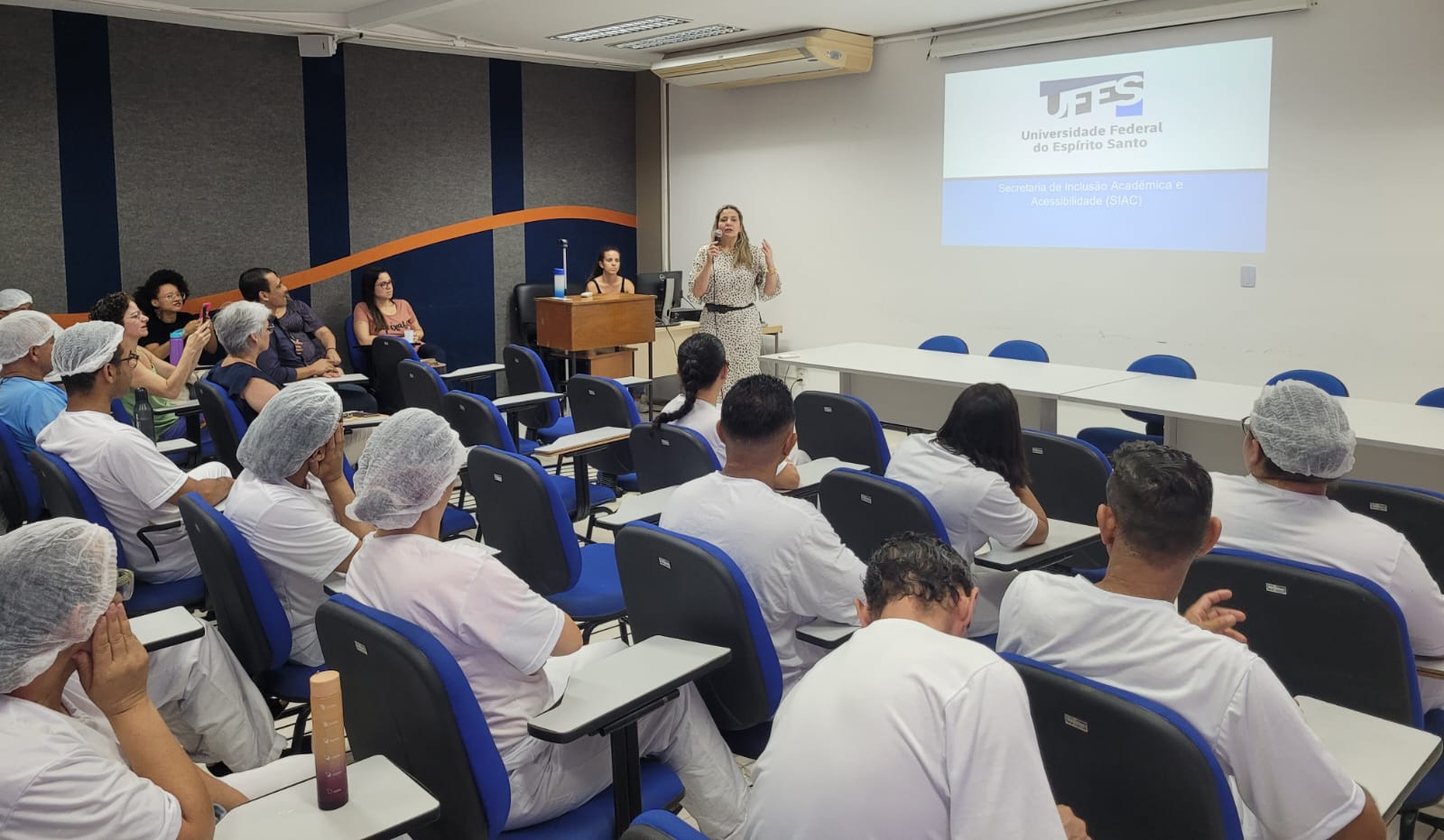 Foto da secretária Cinthya Oliveira falando para os trabalhadores no auditório 