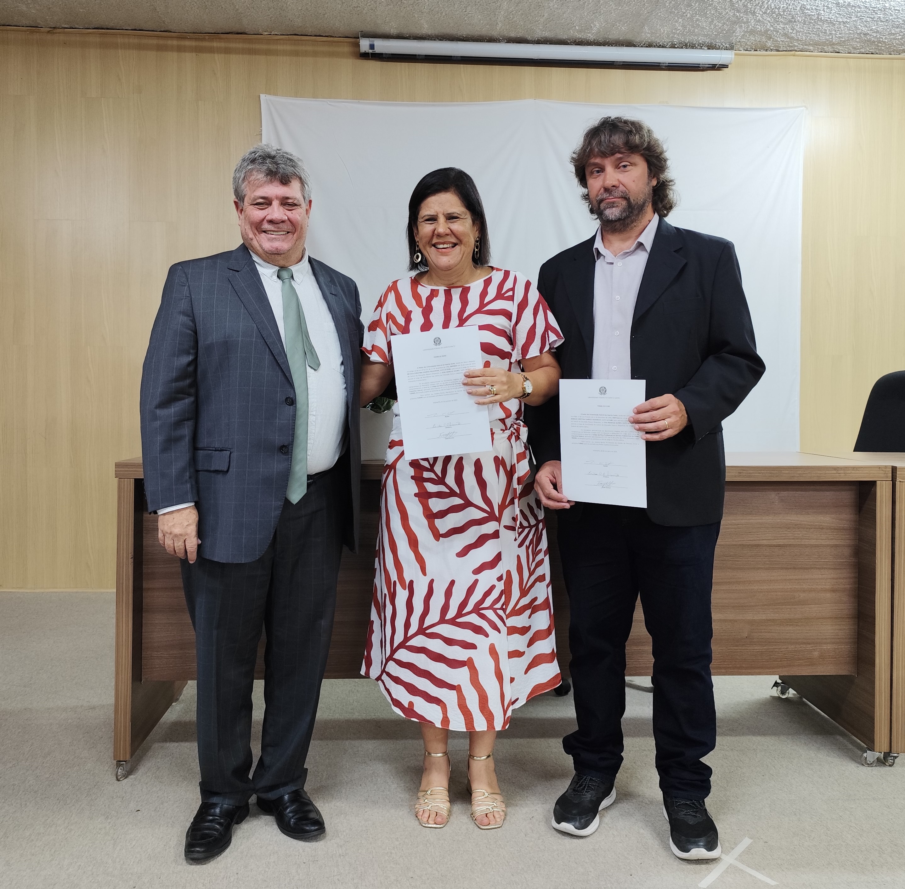 Foto do reitor Eustaquio de Castro, da diretora Zenólia Figueiredo e do vice-diretor Ivan Gomes. A diretora e o vice-diretor mostram o termo de posse