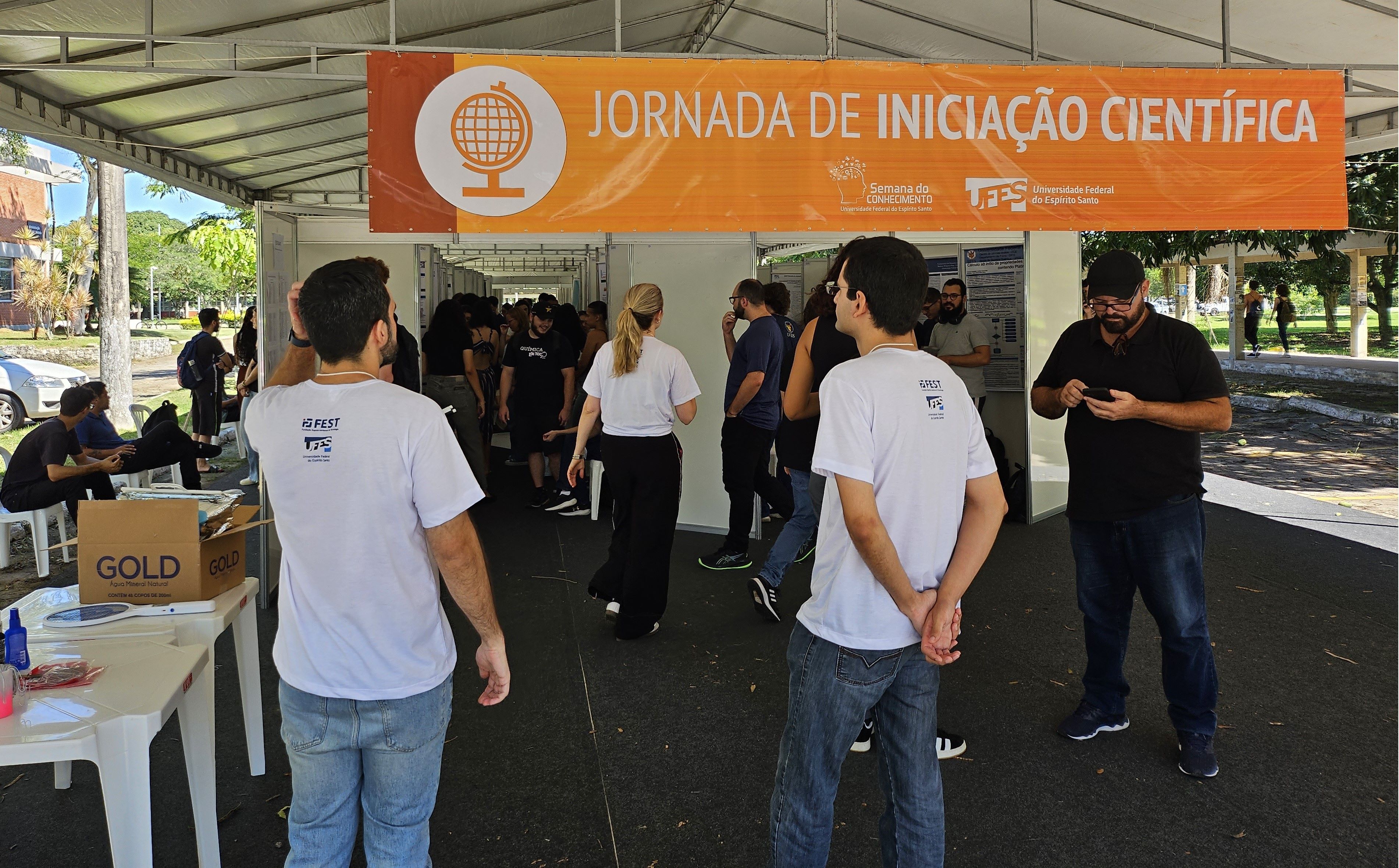 Foto da entrada da tenda, onde há uma faixa na cor laranja, com o nome da Jornada