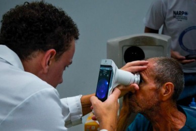 Foto de um médico utilizando um retinógrafo portátil para examinar uma paciente