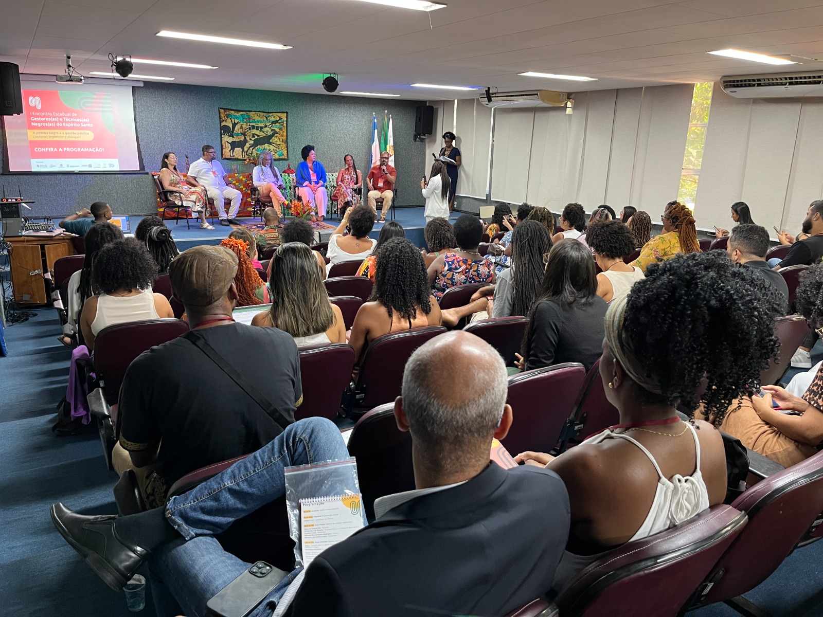 Foto da plateia e da mesa de abertura do evento ao fundo