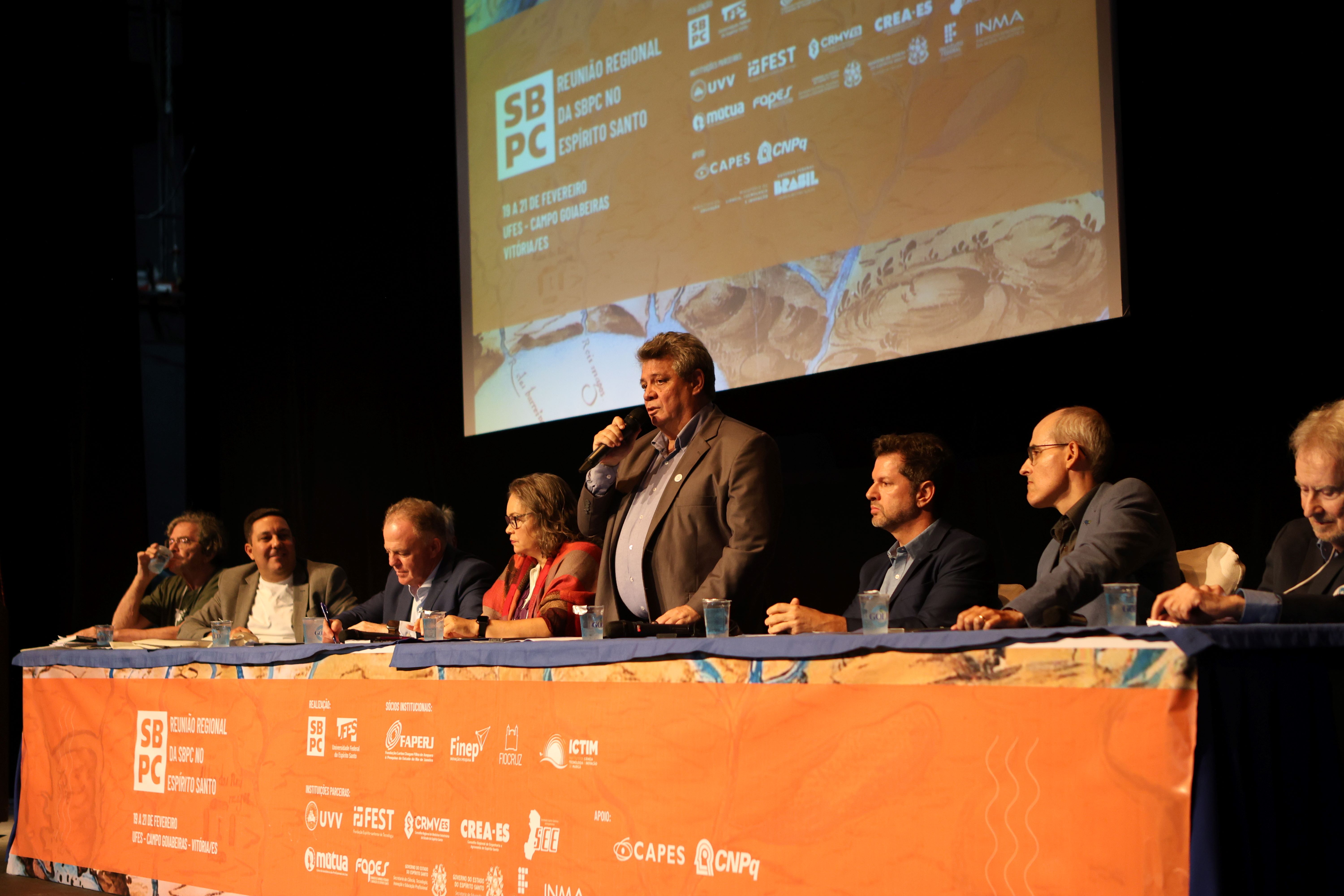 Foto do reitor, na mesa de abertura do evento, falando aos presentes