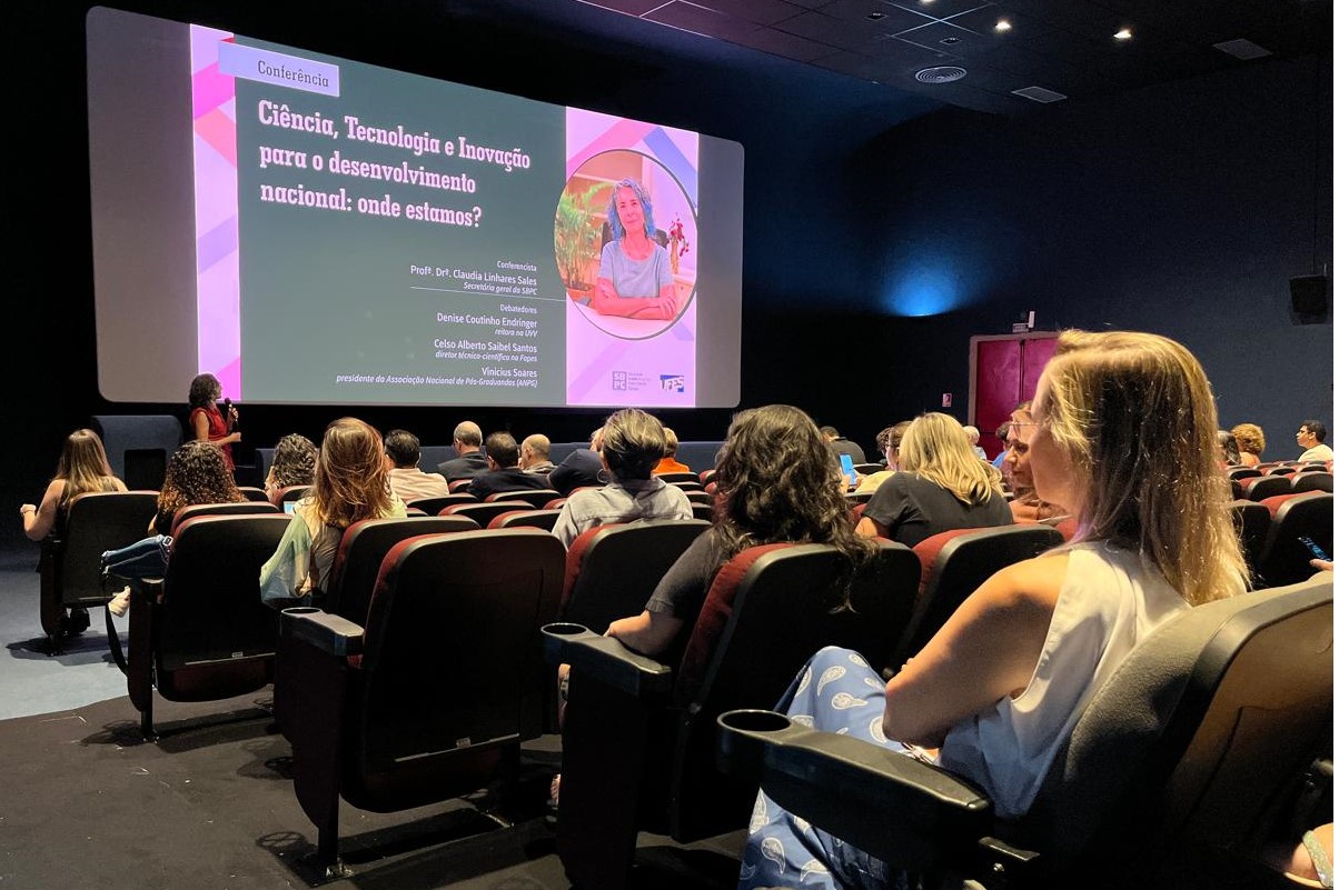 Foto do público assistindo a palestra, com a professora à frente