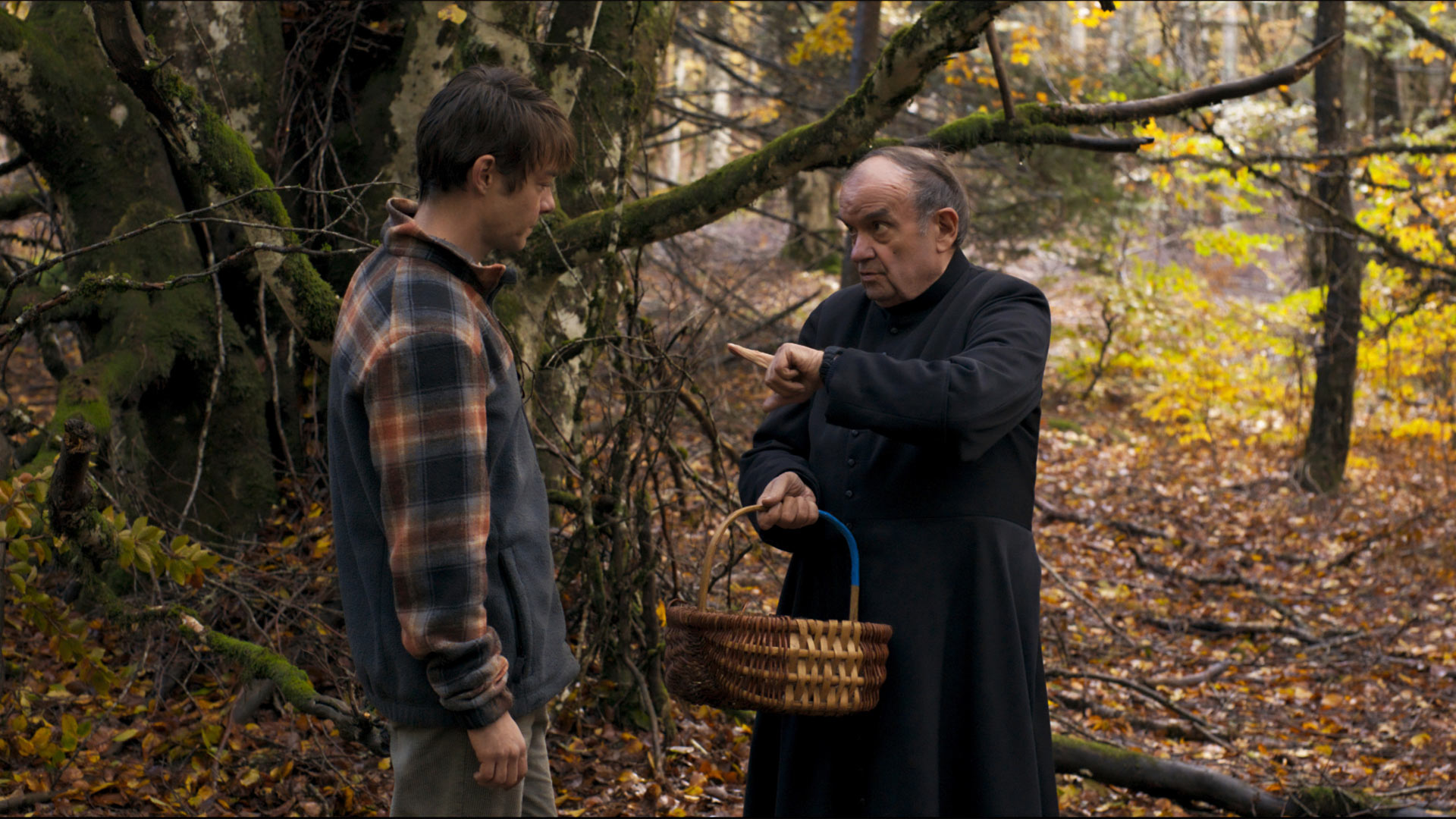 Cena do filme Misericórdia, onde um padre aponta o dedo para um jovem. Ambos estão em uma mata.