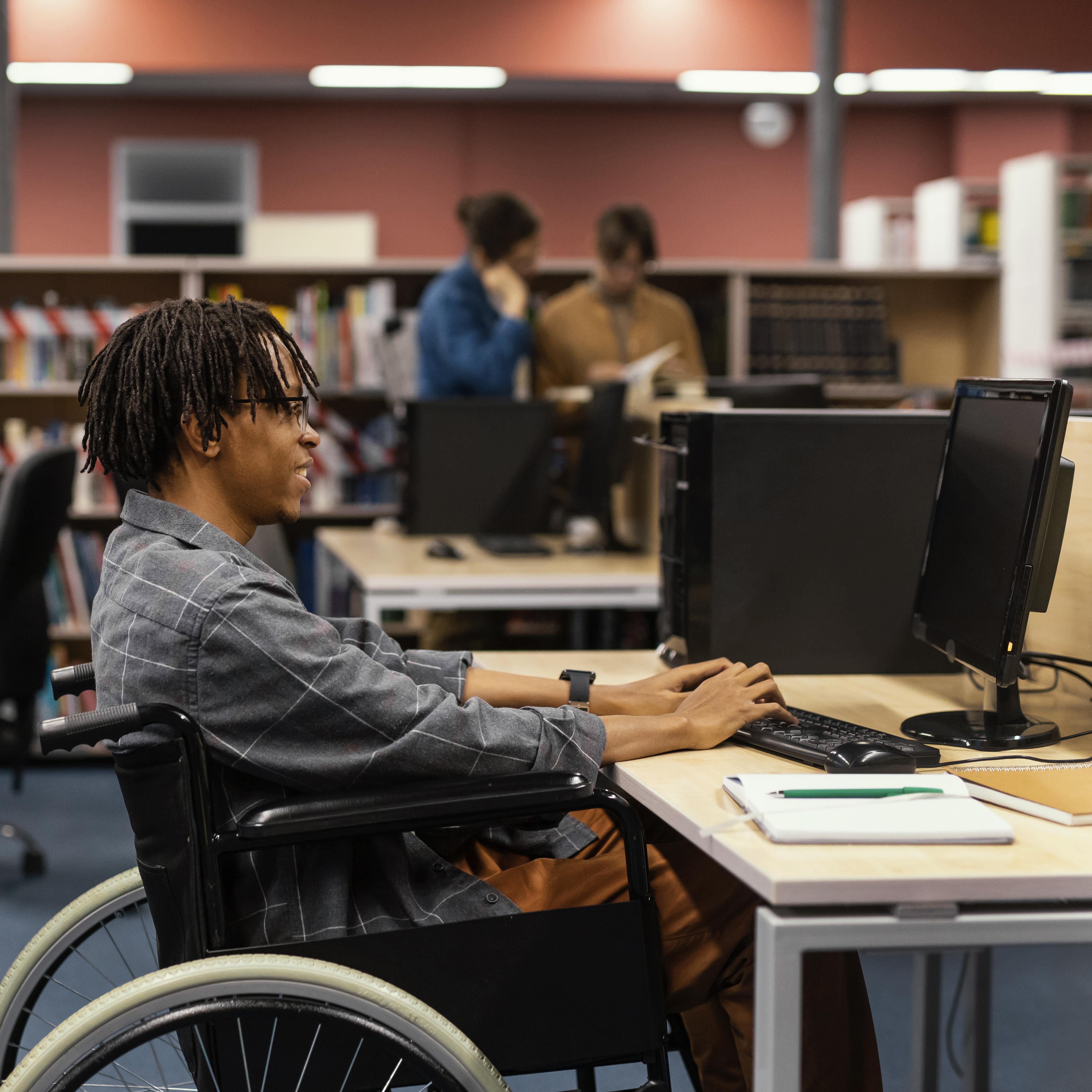 Imagem de um jovem negro em uma cadeira de rodas estudando em uma biblioteca