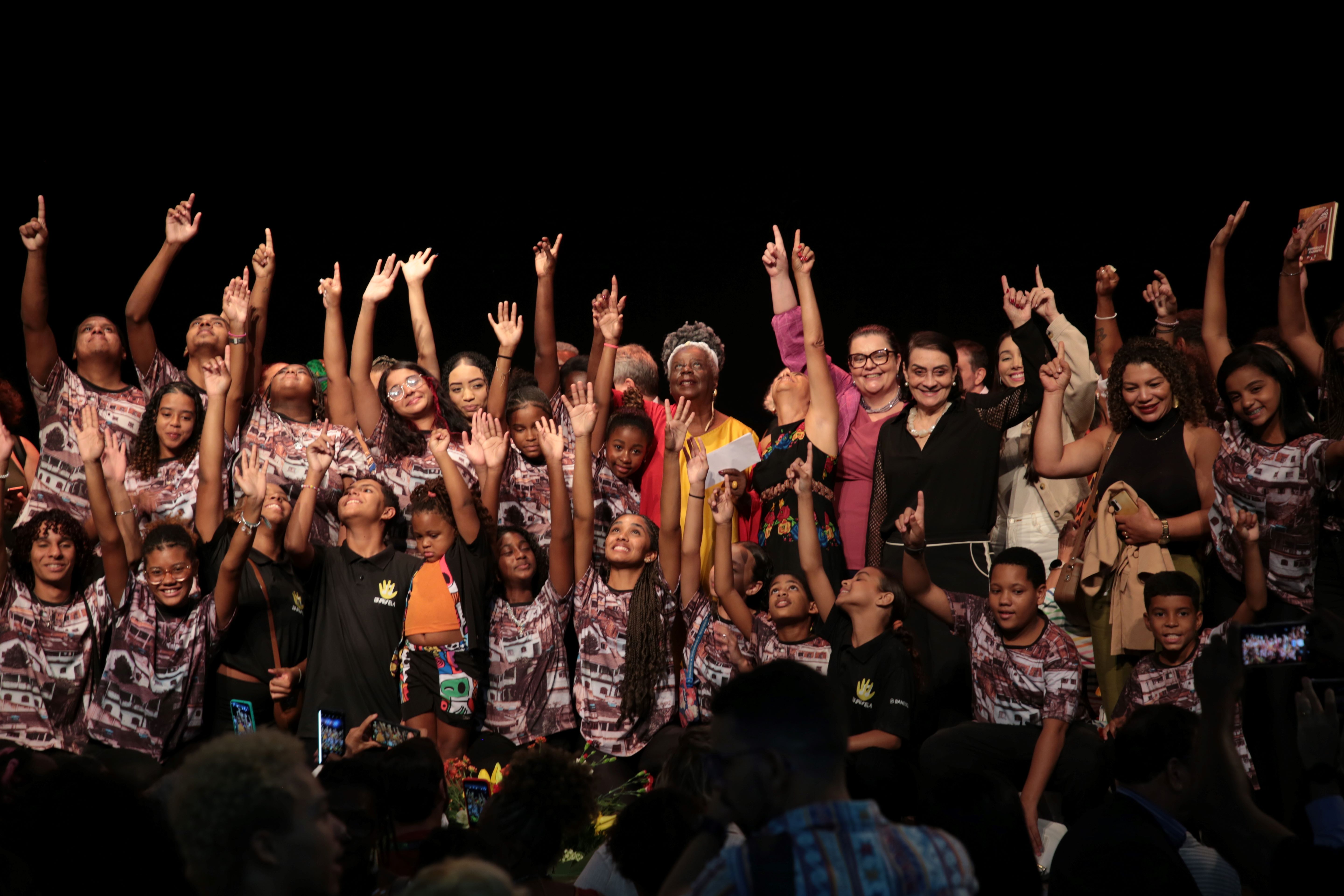 Foto de Conceição Evaristo posando para foto com as crianças do coral do Instituto Serenata D'Favela