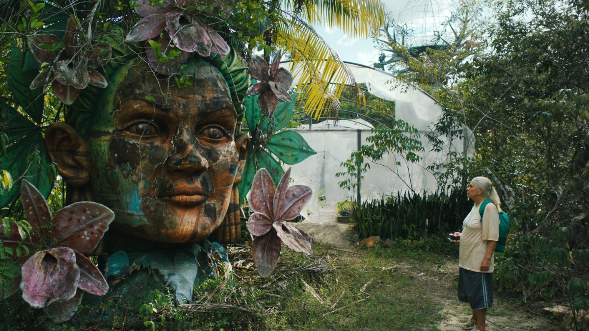 Cena de O Último Azul em que a protagonista aparece olhando a escultura de uma cabeça na floresta