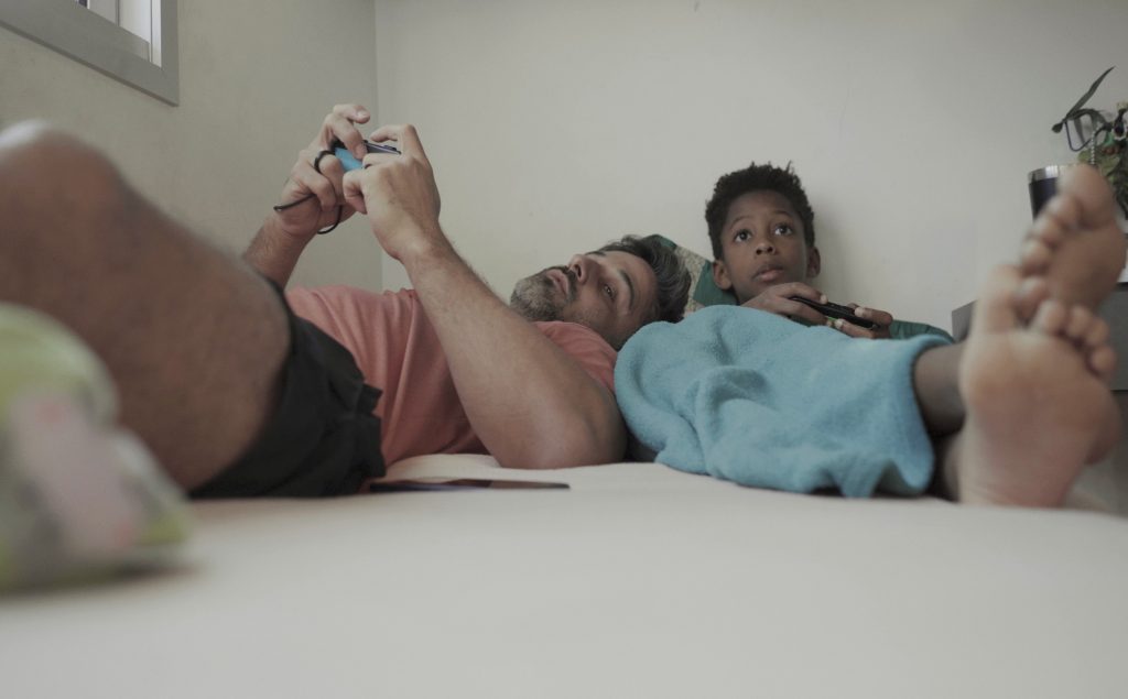 Cena de Lar, na qual aparecem um rapaz e um menino jogando videogame deitados em uma cama