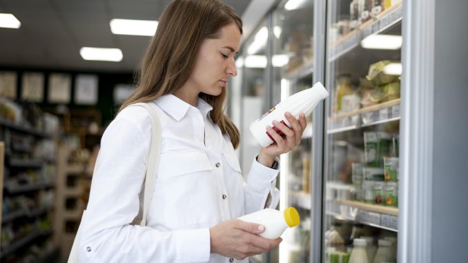 Foto de mulher branca no supermercado olhando rótulo de produto parecido com uma garrada de iogurte