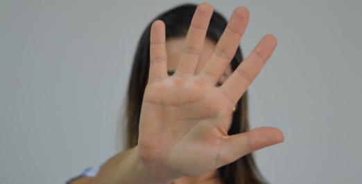 Foto de uma mulher cobrindo o rosto com a mão espalmada em sinal de "basta"