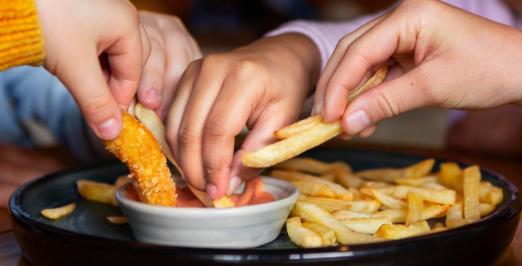 Imagem de mãos de crianças pegando batatas fritas em uma porção