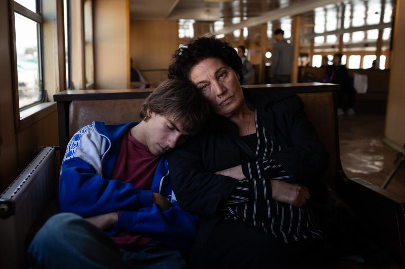 Cena do filme Caminhos Cruzados, na qual aparece o jovem Achi sentado, dormindo no ombro da personagem Lia