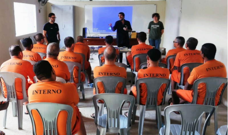 Foto de uma das aulas do projeto com os detentos, de costas, ouvindo a explicação dos professores 