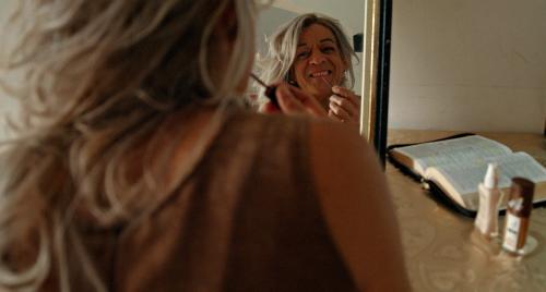 Foto do filme Toda Noite Estarei Lá com a personagem Mel se maquiando diante de um espelho. Ao lado, uma Bíblia.