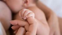 Imagem de um bebê sendo amamentado, segurando no dedo da mãe
