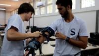 Foto de dois rapazes testando um braço mecânico desenvolvido dentro do Espaço