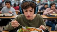 Imagem de um jovem almoçando em um self-service, usando um abafador de ruídos