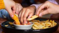 Imagem de mãos de crianças pegando batatas fritas em uma porção