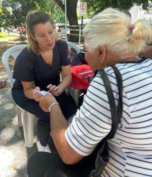 Foto de uma estudante entregando um papel com orientações a uma senhora