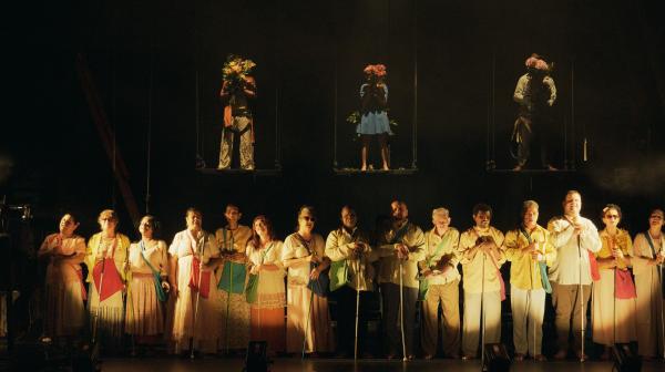 Foto dos membros da orquestra no palco, em uma apresentação onde cantam em pé