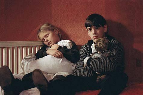 Cena de Fanny e Alexander na qual os protagonista aparecem sentados em um sofá. A menina abraça um travesseiro enquanto o menino abraça um urso de pelúcia