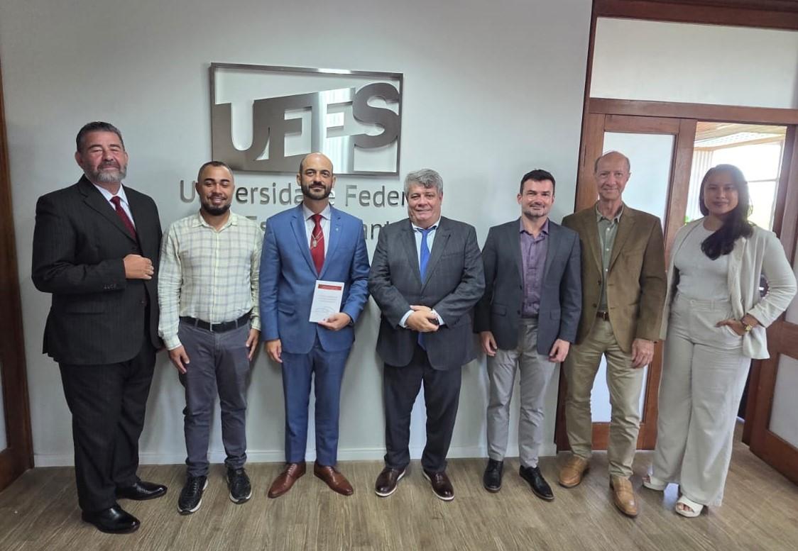 Foto dos participante da reunião em frente a uma parede onde está instalada a logomarca da Ufes