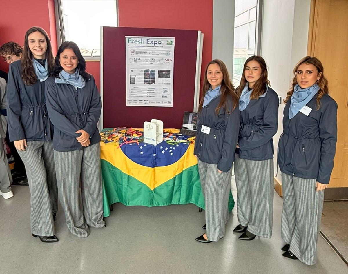 Foto da equipe envolta de uma mesa coberta com a bandeira do Brasil e o prêmio sobre ela