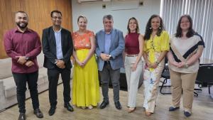 Foto dos participantes da reunião em pé, na sala de reuniões da Reitoria