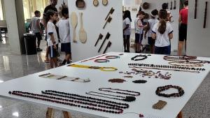 Foto de uma mesa com peças da exposição e os alunos ao fundo