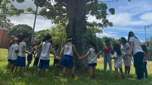 Foto de crianças de mãos dadas em volta de uma árvore, em uma das atividade do Núcleo